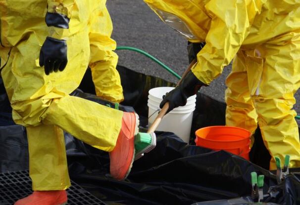 Hazmat cleanup crew in all yellow hazmat suits cleaning hazardous spill on public roadway